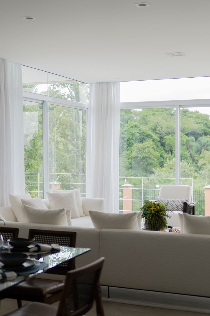 A spacious, bright living room featuring large windows overlooking lush greenery and a comfortable seating area.